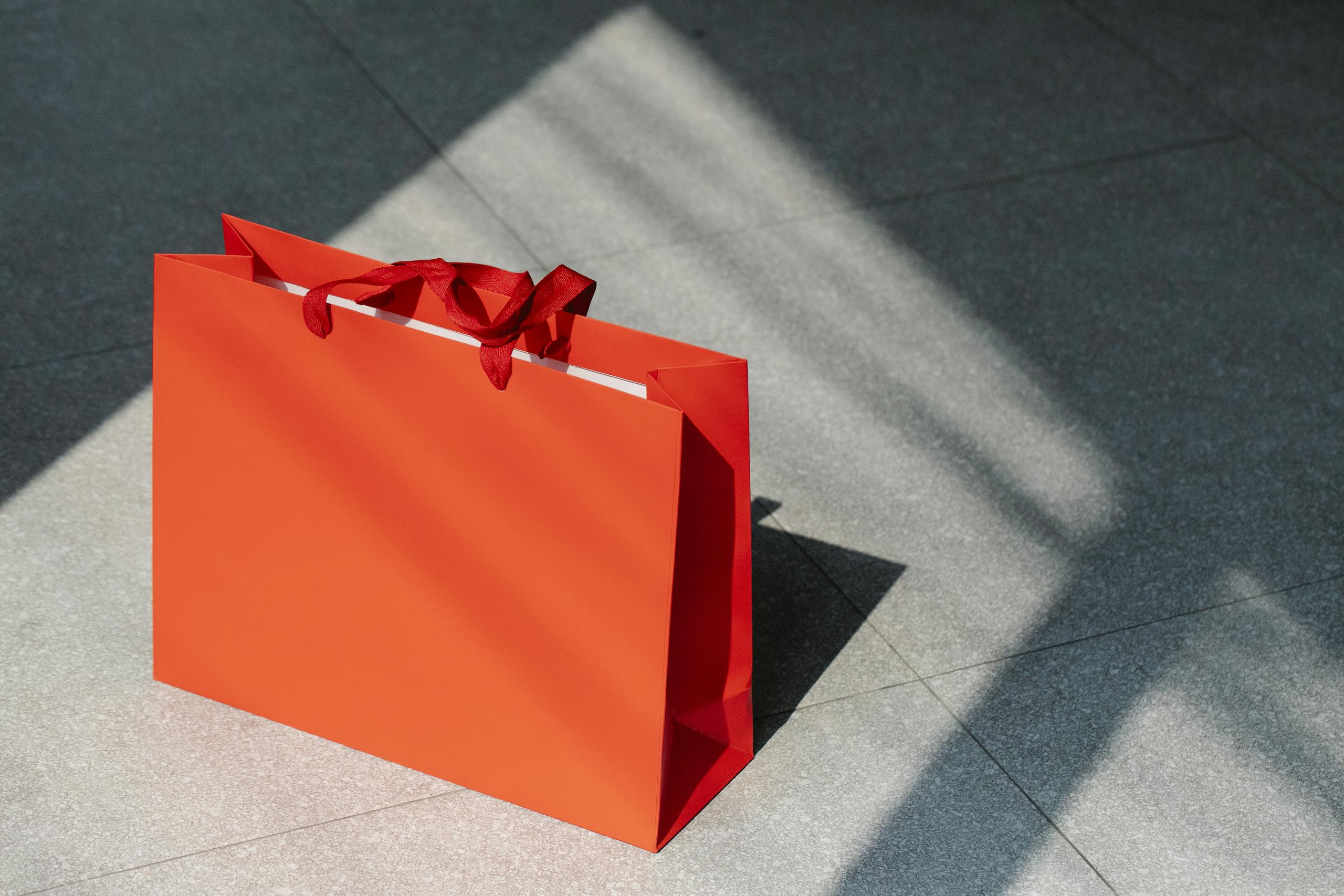 Bright red paper bag on pavement surface under sunlight, ideal for shopping concepts.